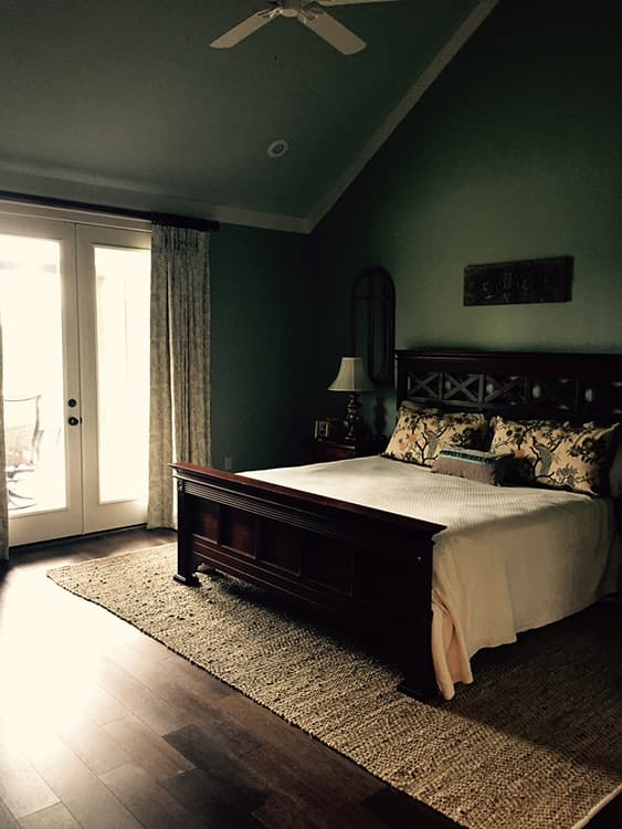 Bedroom interior with vaulted ceiling, French doors, dark wood furniture, and a ceiling fan.