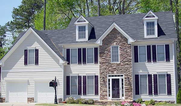 Two-story house plan exterior with vinyl siding, stone facade, dormer windows, and a two-car garage.