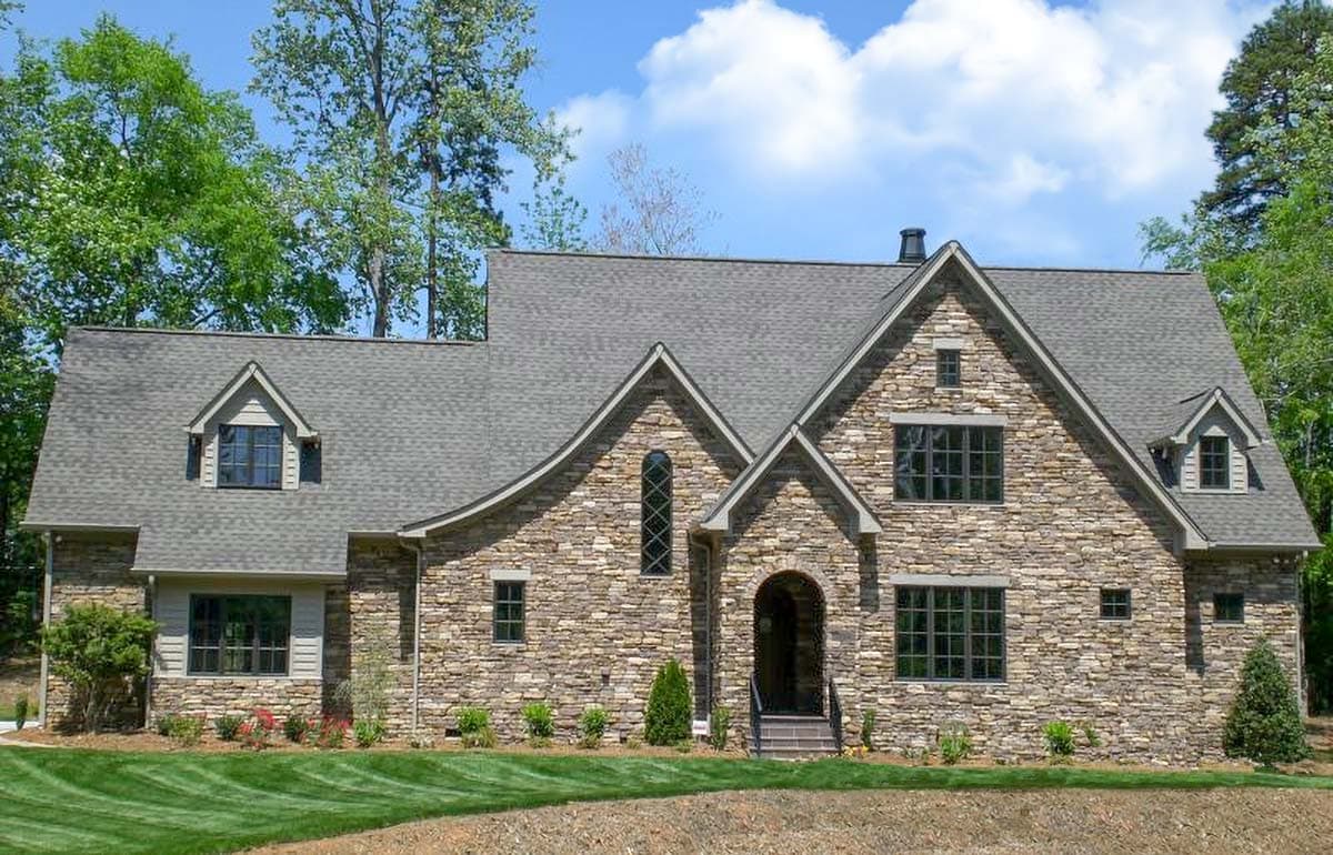 House plan exterior with stone veneer, gabled roof, and arched entry. Features include dormers and multiple window styles. Two-story design.