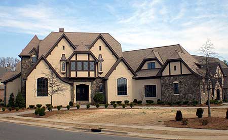 House plan exterior: Tudor style, two-story home with stone accents, multiple gables, and a prominent bay window.