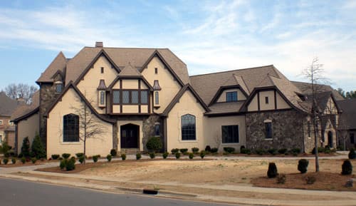 House plan exterior featuring Tudor style with stone accents, multiple gables, and a prominent bay window above the entrance.
