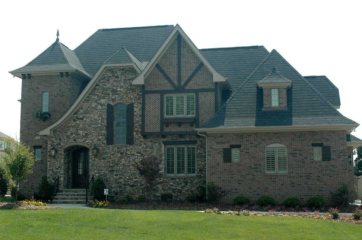 House plan exterior with stone and brick facade, multiple gables, arched entryway, and dormer windows.