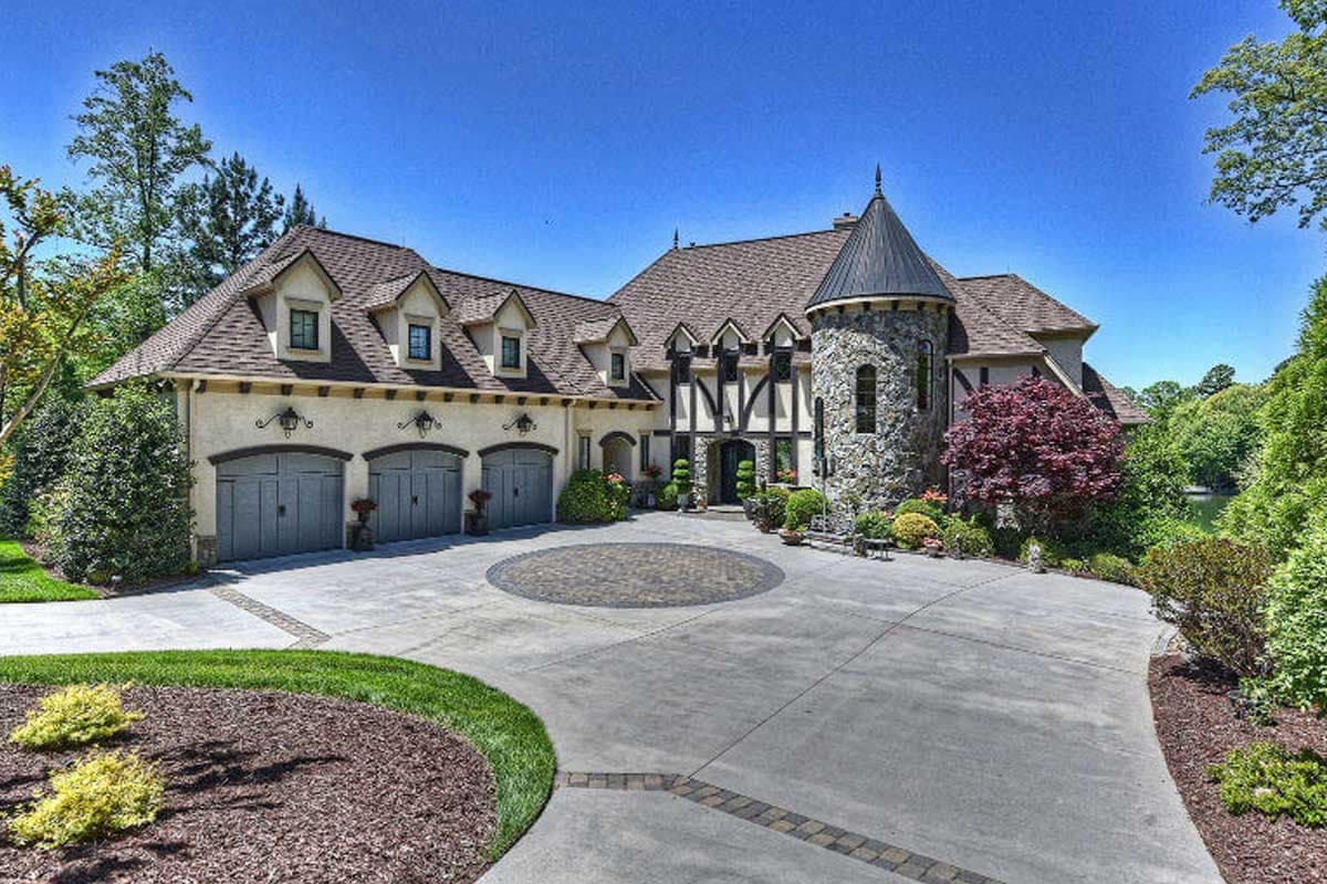 House plan exterior. Two-story Tudor style home with stone turret, dormers, and a three-car garage. Features a circular driveway.