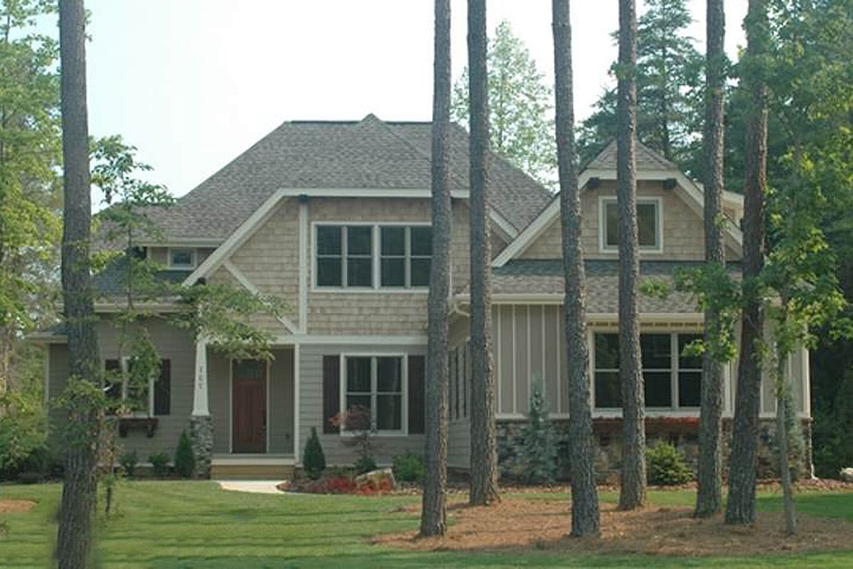House plan exterior: Two-story home with shingle siding, stone accents, gables, dormers, and covered front porch.