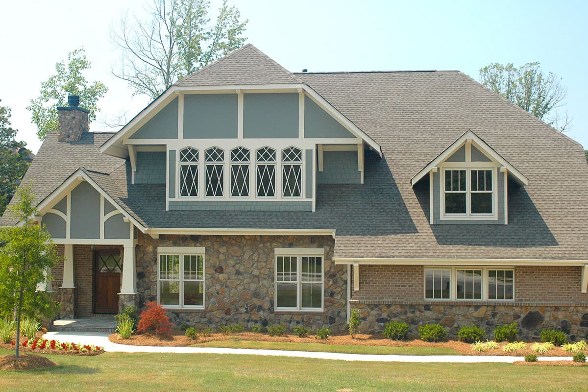 House plan exterior with stone and brick facade, multiple gables, dormers, and decorative diamond-pattern windows.