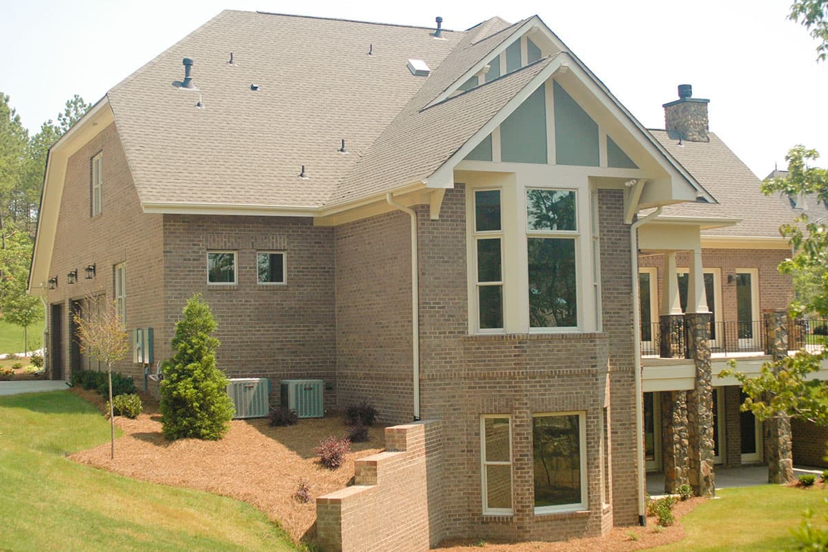 House plan exterior: Brick two-story home with side-entry garage, multi-level rooflines, large bay window, and stone column porch.