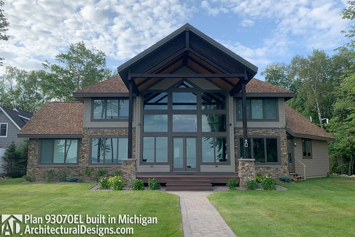 House plan exterior: Two-story home with a prominent gable, large glass facade, stone accents, and covered entryway.