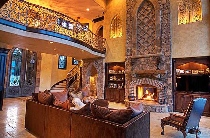 Great room with vaulted ceiling, stone fireplace, wrought iron balcony, and spiral staircase.