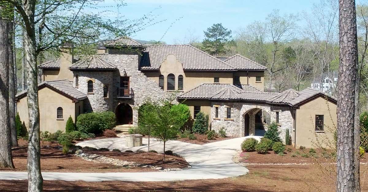 House plan exterior. Two-story Mediterranean style with stone facade. Features arched entries, tile roof, and multiple gables.