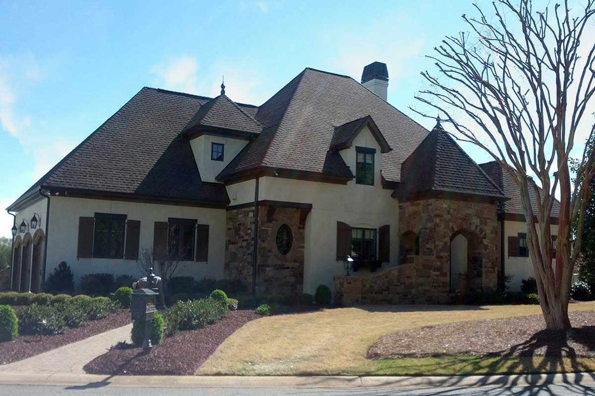 House plan exterior. Two-story with stone facade, multiple gables, and a turreted entry. Features include a prominent roofline and arched doorway.