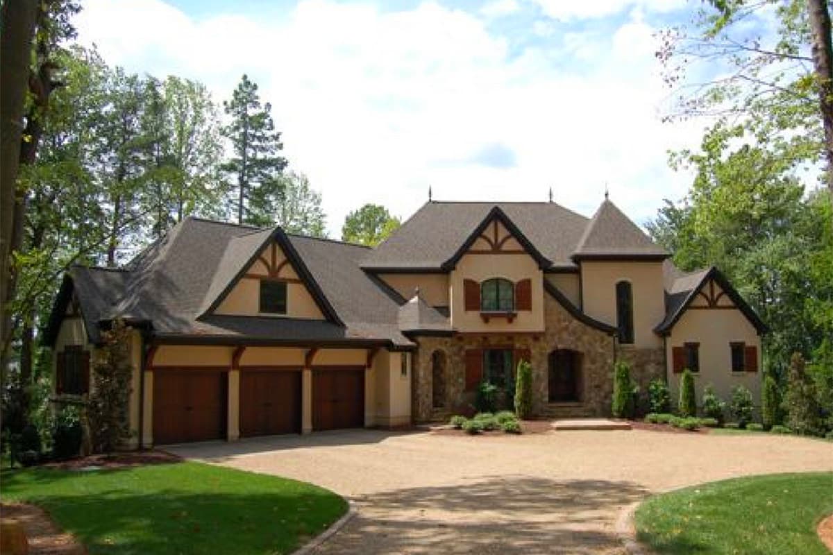 House plan exterior. Tudor style, two stories, with a three-car garage, prominent gables, and stone accents.