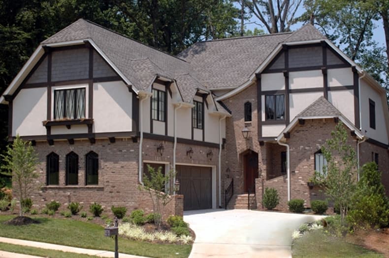 Tudor-style house plan exterior with brick facade, decorative half-timbering, multiple gables, and a side-entry garage.