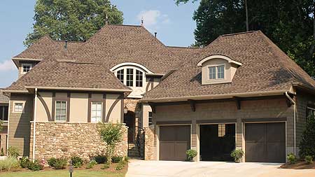 House plan exterior with stone base, multiple gables, arched dormer window, and a three-car garage.