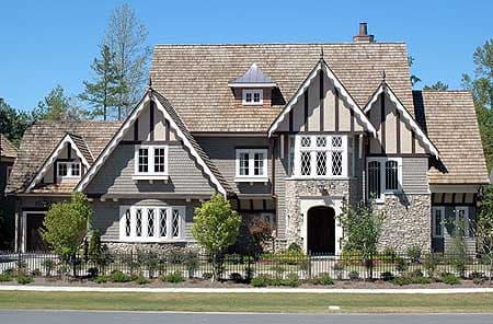 Tudor-style house plan exterior with multiple gables, stone and shingle siding, and diamond-paned windows.