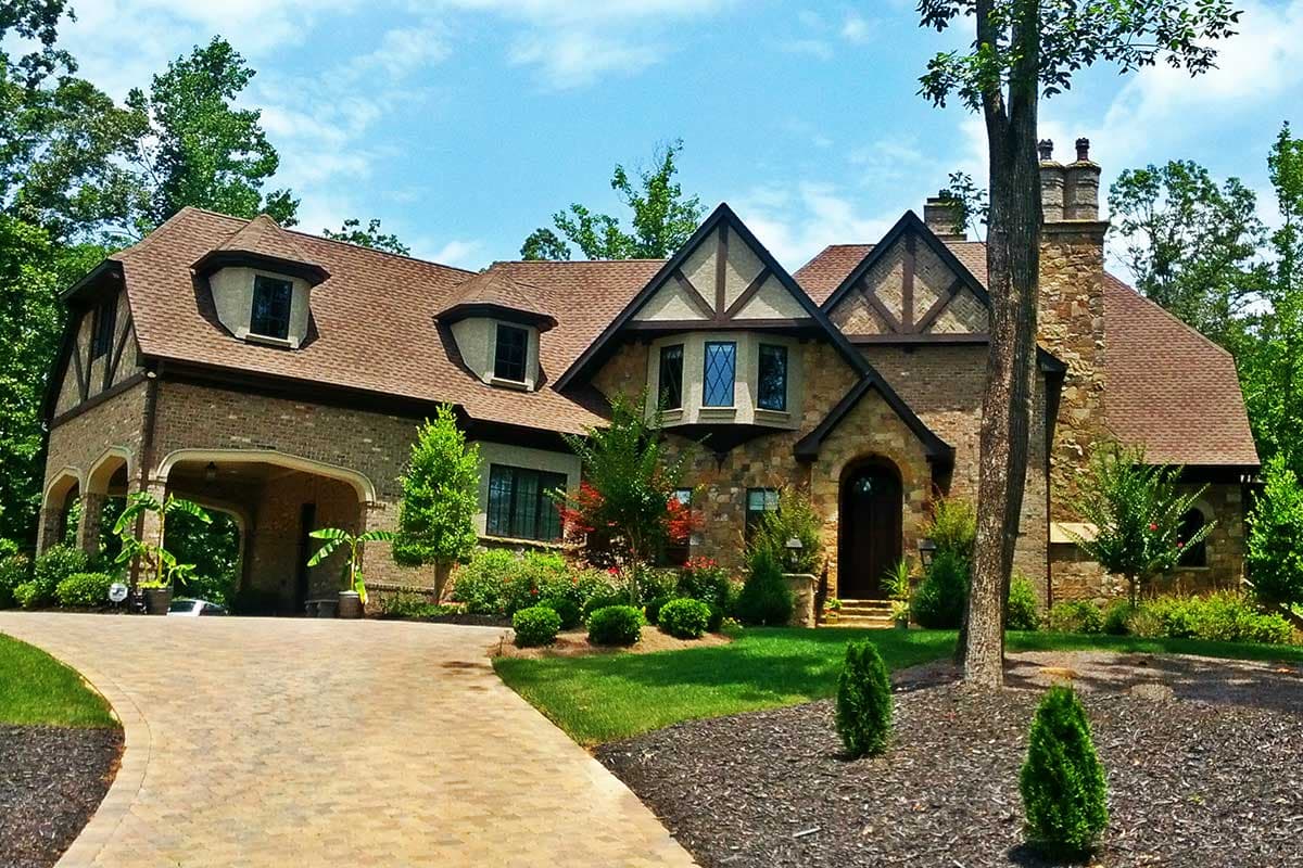 House plan exterior in Tudor style with gabled rooflines, dormers, and an arched porte-cochere. Two-story structure with stone and brick facade.