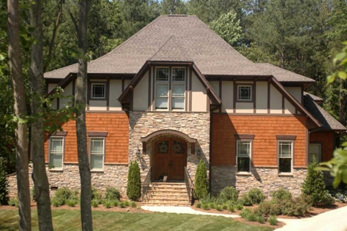 House plan exterior. Two-story Tudor style home with stone facade and gabled roof. Features include an arched entryway and wood shake siding.