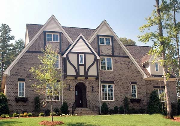 Tudor-style house plan exterior with multiple gables, brick facade, and decorative half-timbering around the arched entryway.