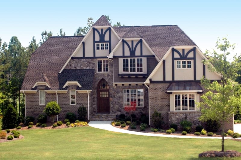 House plan exterior with stone and brick facade, multiple gables, decorative half-timbering, and arched entry.