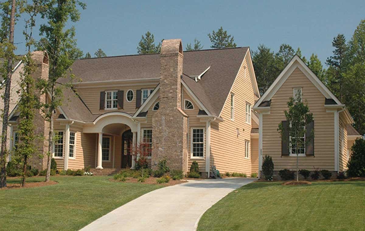 House plan exterior with a prominent brick chimney, arched entryway, gables, and multiple rooflines.