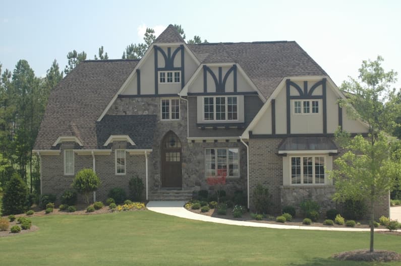 Tudor-style house plan exterior with stone and brick facade, prominent gables with dark trim, and multi-pane windows.