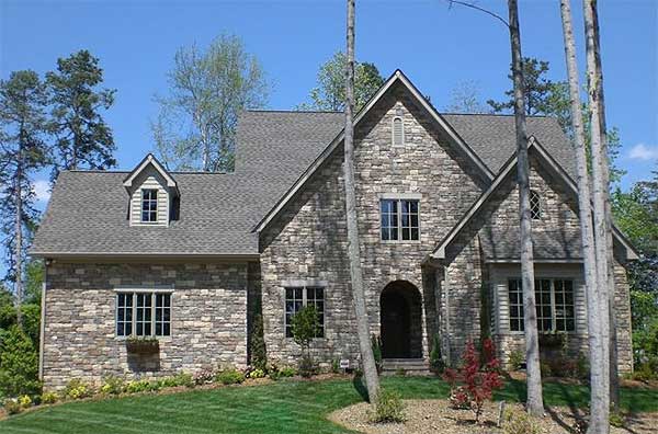 House plan exterior: Stone facade, steeply pitched roof with gables, dormer, and arched entryway.
