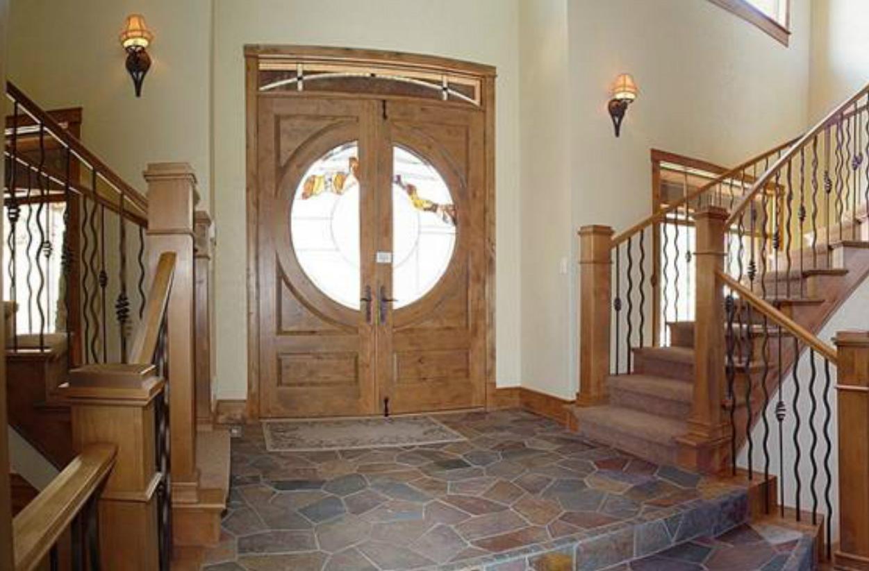 Foyer with double wooden doors featuring circular leaded glass, slate floor, and curved staircase with metal balusters.