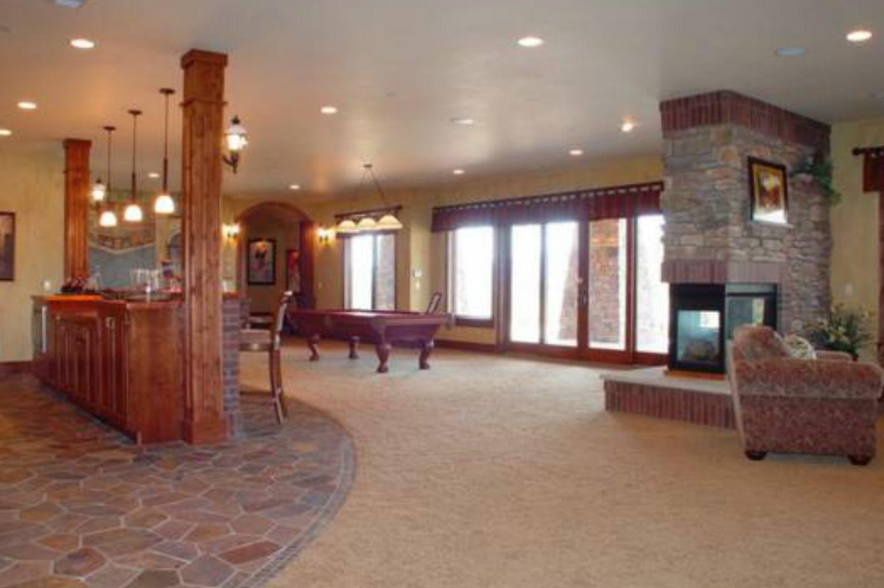Interior view of finished basement with wood bar, pool table, stone fireplace, and large sliding glass doors.