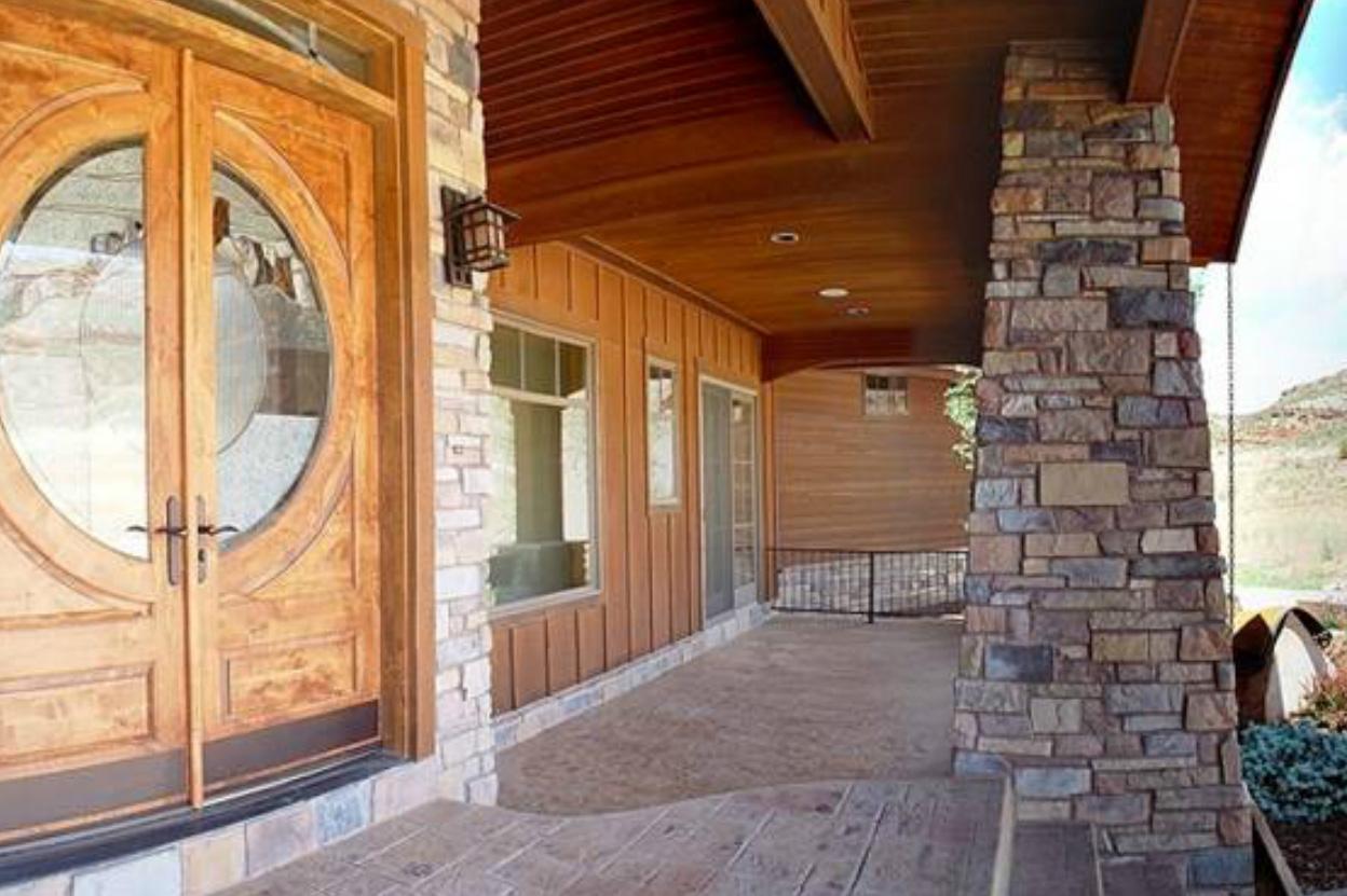 House plan exterior with double wood doors, stone accents, and covered porch with wood ceiling and stone column.