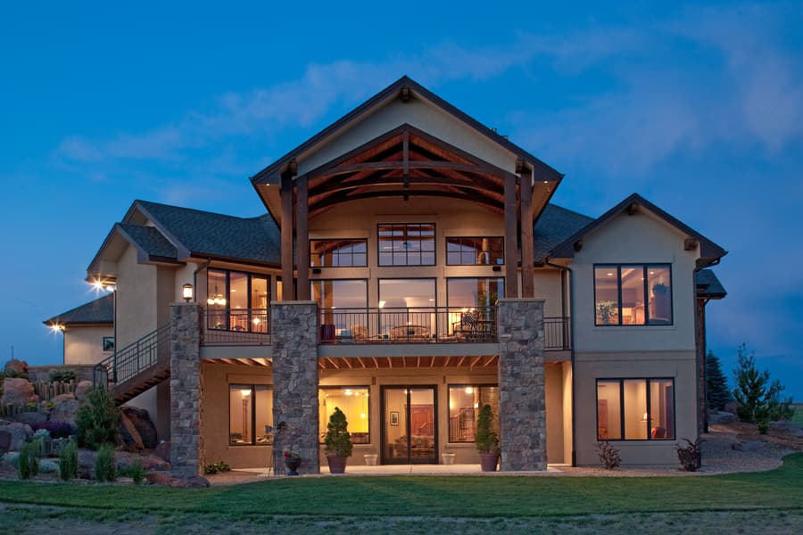 Modern house plan exterior with stone pillars, large windows, multi-level balconies, and exposed timber roof beams.