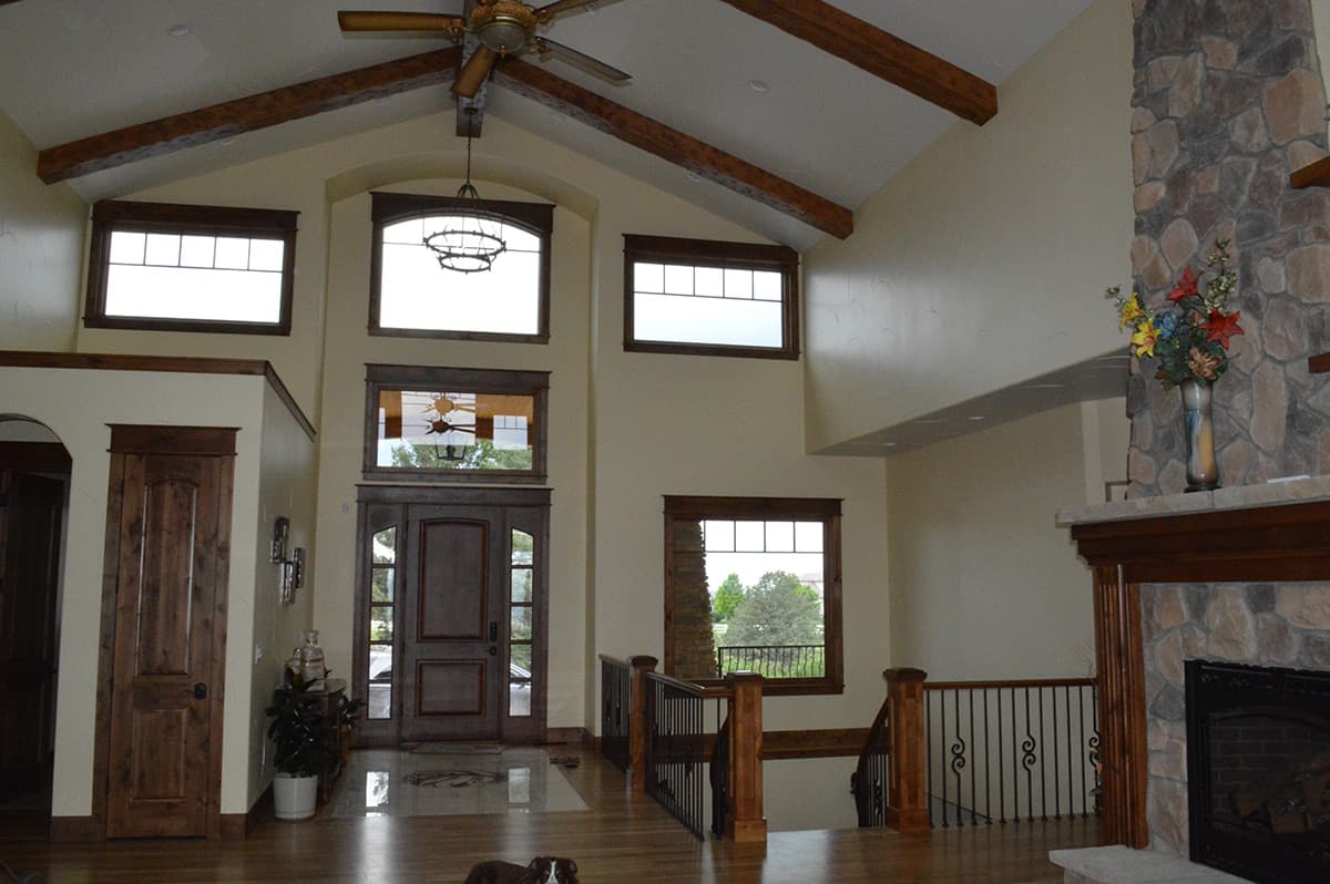 Interior view of home with vaulted ceiling, exposed beams, stone fireplace, grand staircase, and double entry doors.