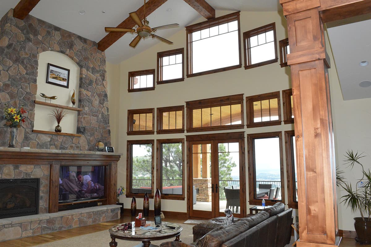 Interior view of a great room with a large stone fireplace, vaulted ceiling with exposed beams, and multiple wood-trimmed windows.