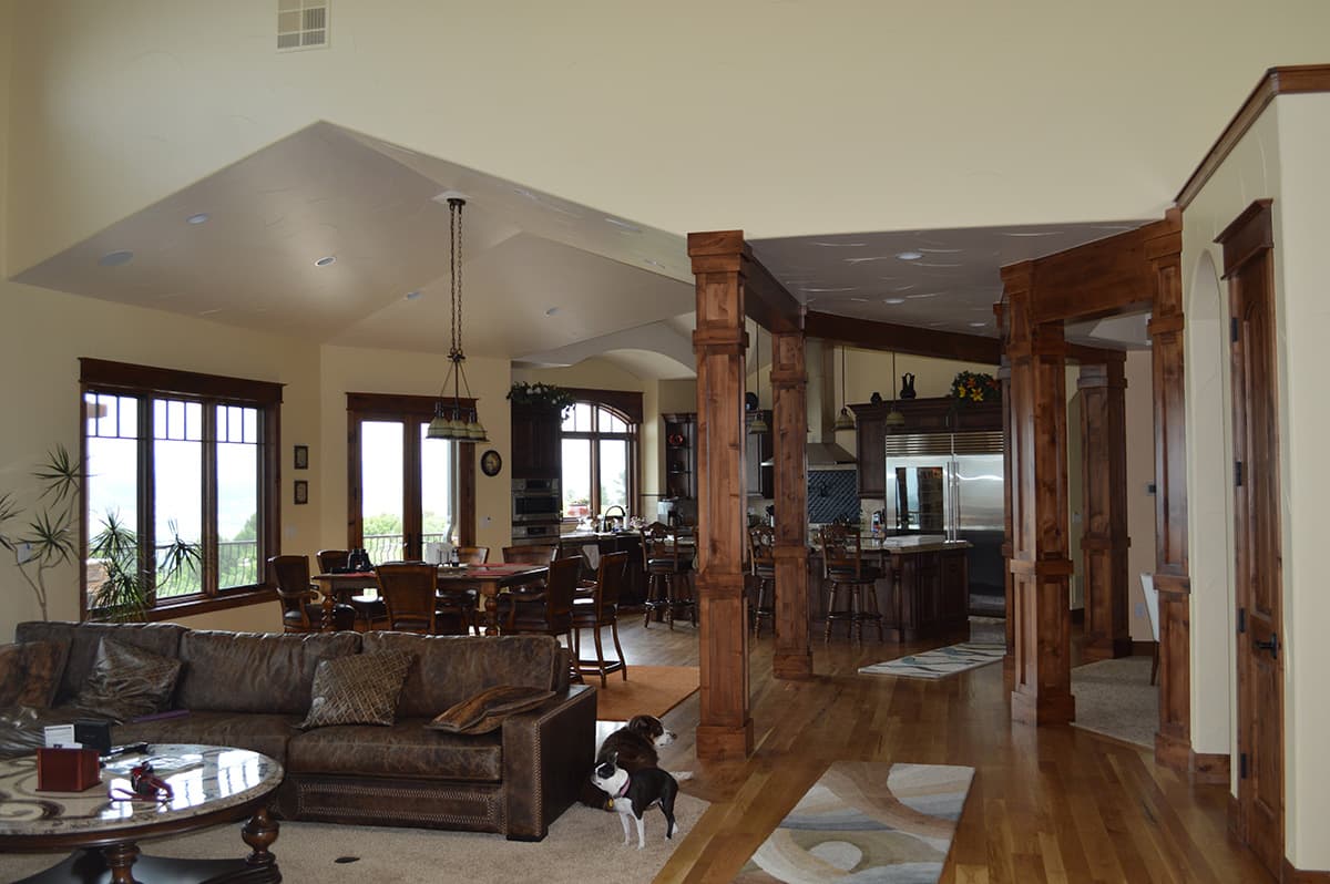 Interior view of open-concept living, dining, and kitchen with vaulted ceiling, wood beams, island, and leather sofa.