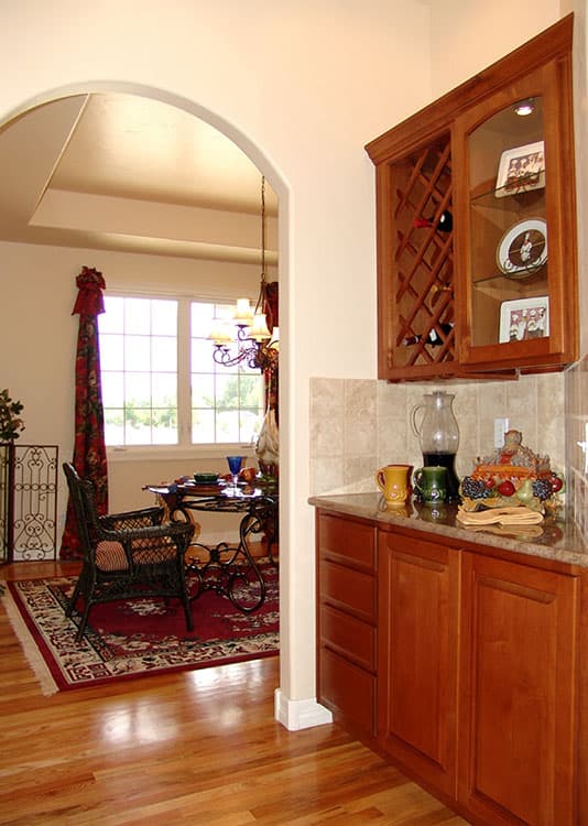 Interior view of kitchen and dining area with arched doorway, wooden cabinets, wine rack, and chandelier.