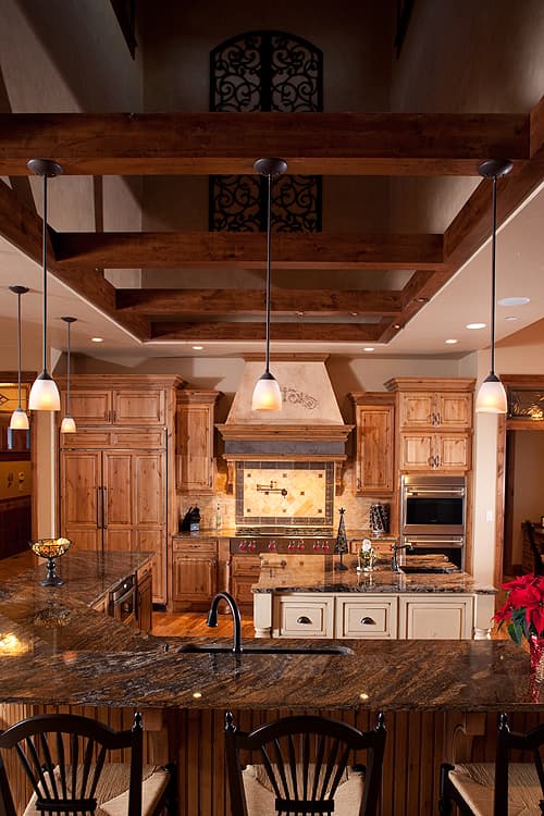 Kitchen with wood beam ceiling, granite countertops, wood cabinetry, and a large island with sink and pendant lights.
