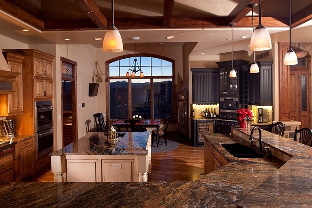 Open concept kitchen featuring dark cabinetry, dual ovens, granite countertops, and large arched window with mountain view.