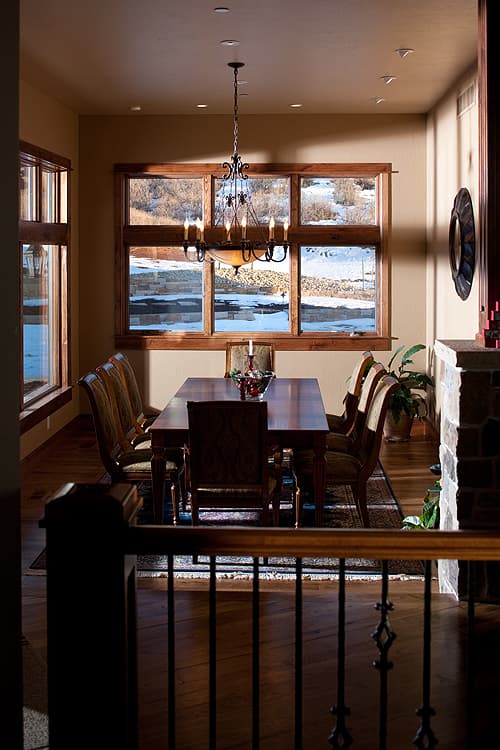 Dining room with a large table, ornate chandelier, and expansive windows overlooking a snowy landscape.