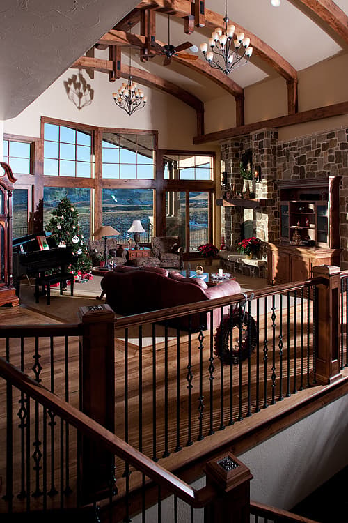 Great room interior with vaulted beamed ceiling, stone fireplace, large windows, and wooden staircase.