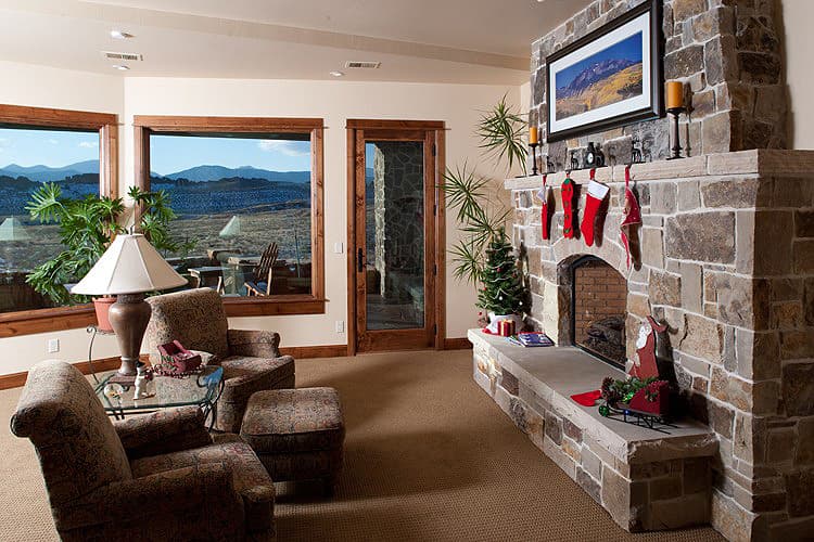 Living room with stone fireplace, large windows with mountain views, and seating area.