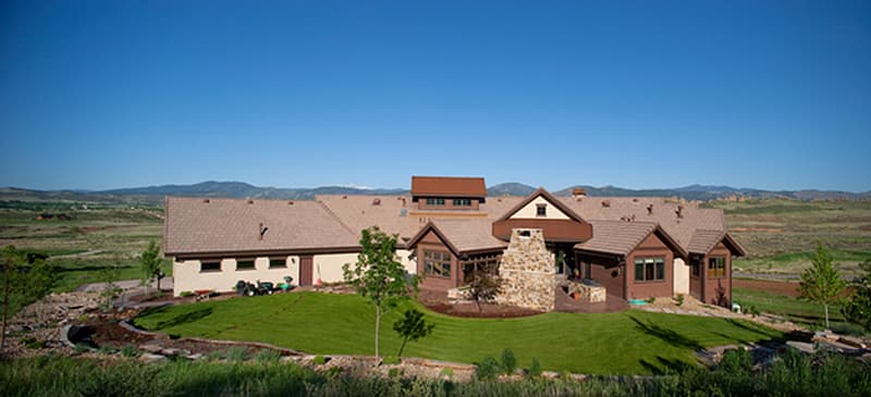 House plan exterior. Two-story home with multiple gabled rooflines, stone chimney, and covered entry. Set on a large, landscaped lot.