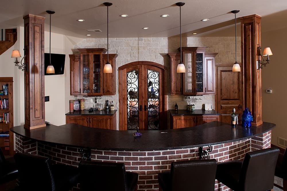 Bar area with a curved brick base, granite countertop, wood cabinetry, and decorative double doors with wrought iron detail.