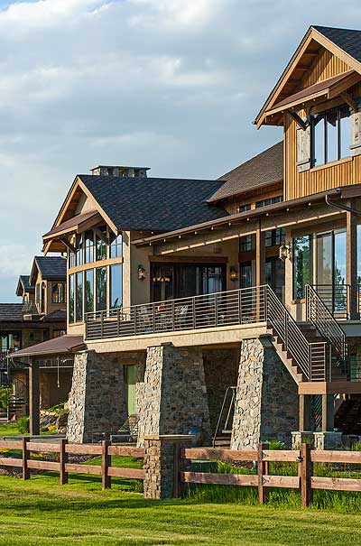 House plan exterior: Modern Lodge style, two stories, stone foundation, expansive deck with metal railing, and prominent gables.