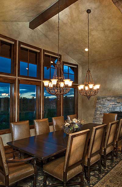 Dining room with large windows, wood beam ceiling, two ornate chandeliers, and leather dining chairs.