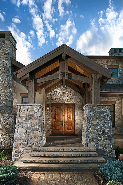 House plan exterior: Rustic stone facade with exposed timber gable roof over double wood doors and stone pillars.