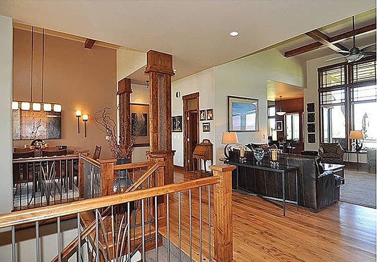 Interior view of open-concept living space with wood beams, a staircase, dining area, and large windows.