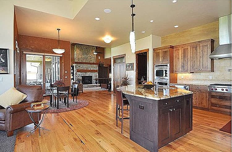 Open concept kitchen and living area with stone fireplace, large island with sink, wood cabinets, and hardwood floors.