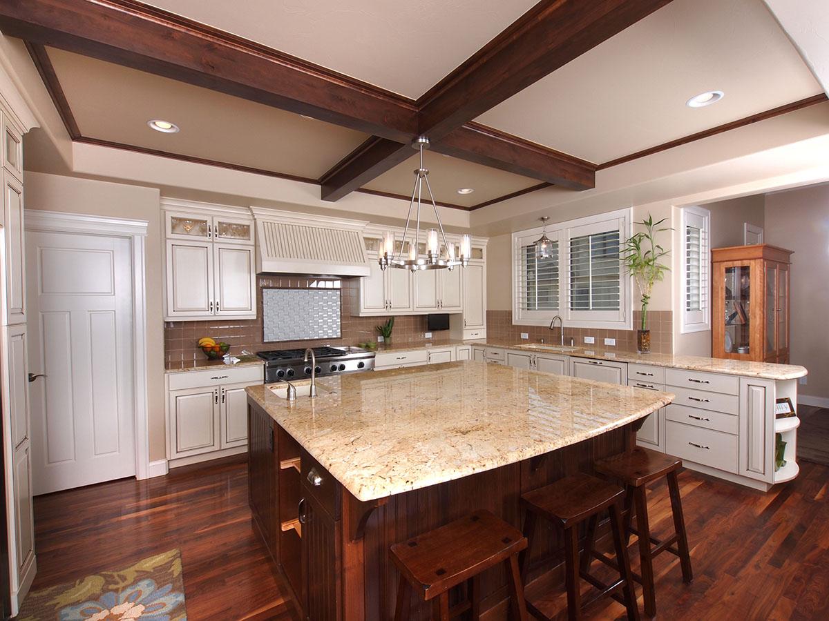 Kitchen interior with a central island, granite countertops, white cabinetry, decorative ceiling beams, and hardwood flooring.
