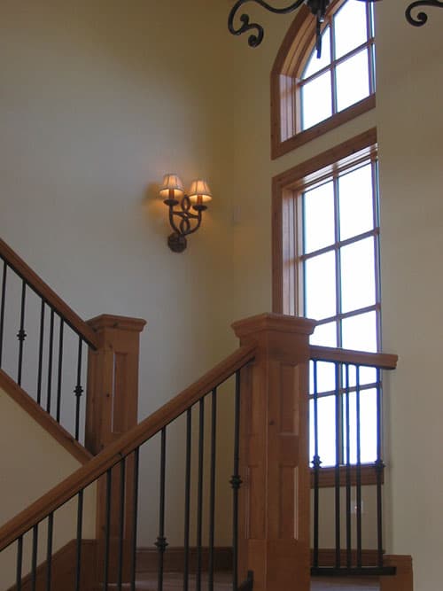 Interior view of a wooden staircase with wrought iron balusters and a three-part arched window.