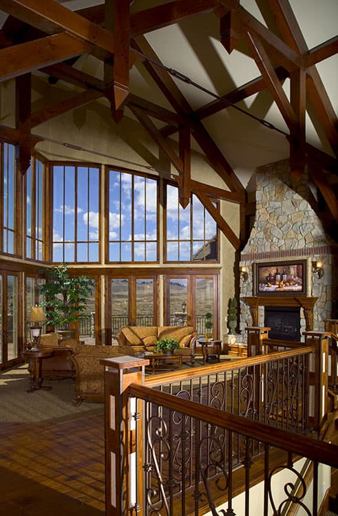 Great room with stone fireplace, vaulted wooden beam ceiling, and floor-to-ceiling windows.