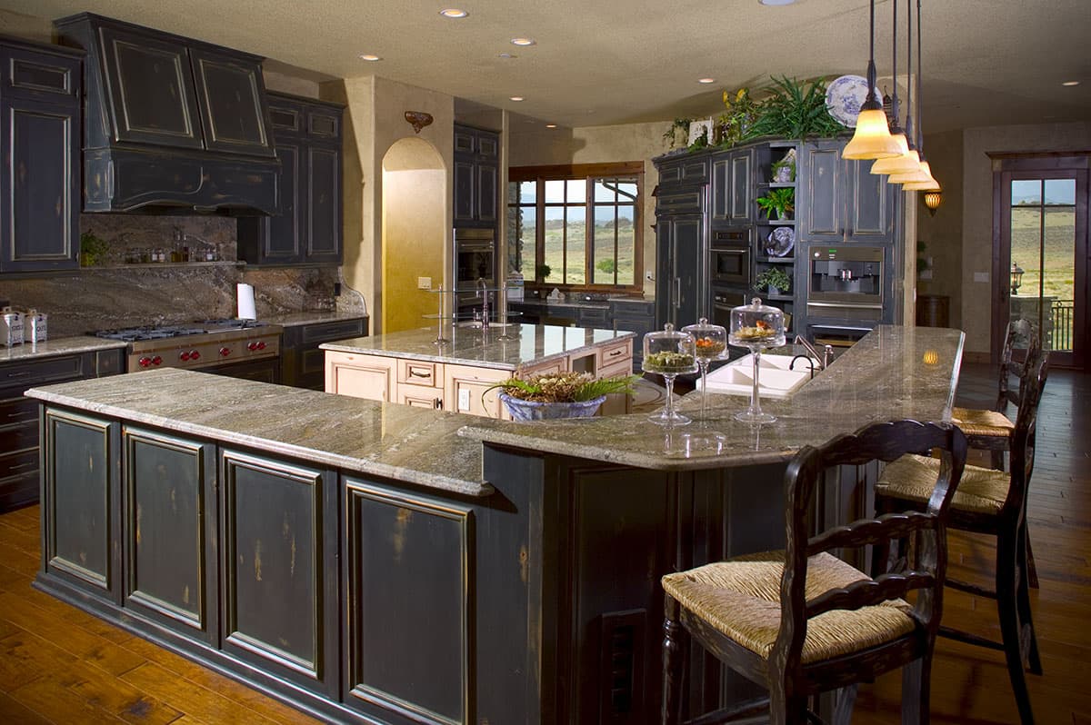 Kitchen featuring dark distressed cabinetry, granite countertops, a large island with seating, and a view of rolling hills through a window.