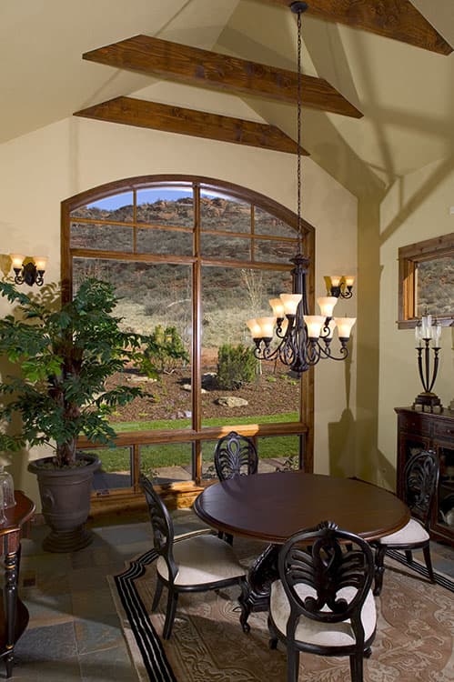 Dining room with oval table, chairs, chandelier, and large arched window with mountain view.